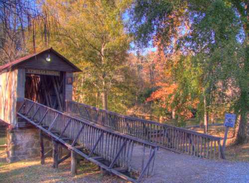 A covered bridge with a wooden ramp, surrounded by trees in autumn colors, leading to a serene landscape.