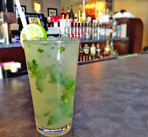 A refreshing mojito with mint and lime, served in a tall glass, with a bar and bottles in the background.