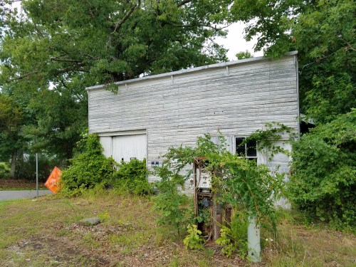 Abandoned building covered in overgrown vegetation, with a weathered exterior and a nearby construction sign.