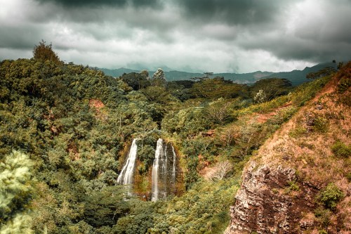 A lush green landscape featuring a waterfall cascading down rocky cliffs under a cloudy sky.
