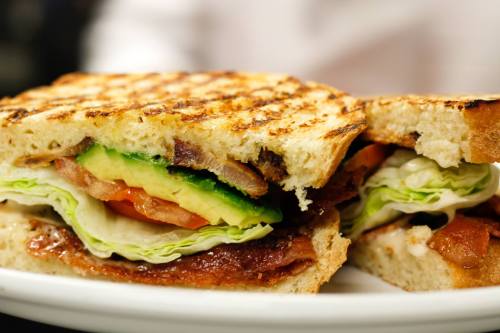 A close-up of a grilled sandwich filled with lettuce, tomato, avocado, bacon, and turkey on toasted bread.