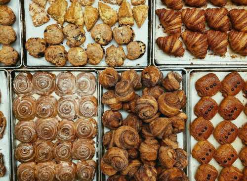 A variety of baked goods arranged on trays, including pastries, croissants, and cookies.