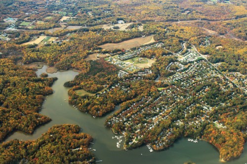 Aerial view of a colorful autumn landscape featuring a lake, wooded areas, and residential neighborhoods.