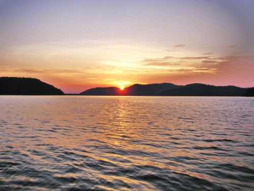 A serene sunset over a calm lake, with silhouettes of hills in the background and vibrant colors in the sky.