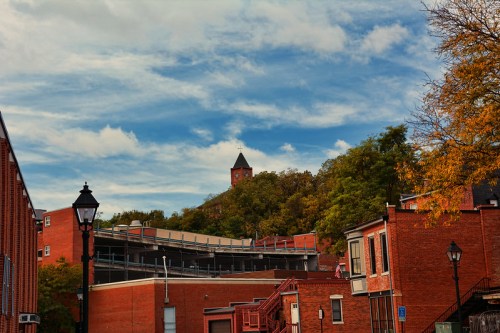A view of red brick buildings with a clock tower on a hill, under a blue sky with scattered clouds.