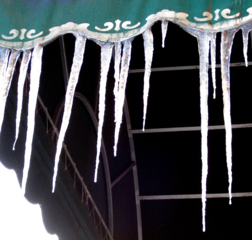 Icicles hanging from a green awning, glistening in the light against a dark background.