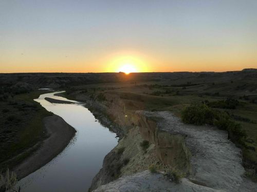 A serene sunset over a winding river, surrounded by rolling hills and open fields.