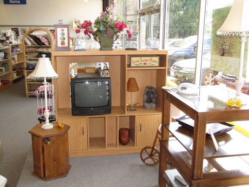 A cozy thrift store display featuring a wooden shelf, vintage TV, decorative items, and a lamp.