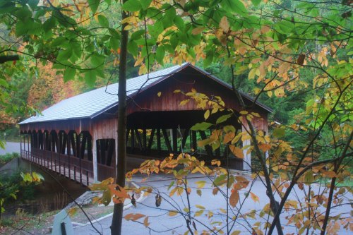 A wooden covered bridge surrounded by colorful autumn leaves and trees.