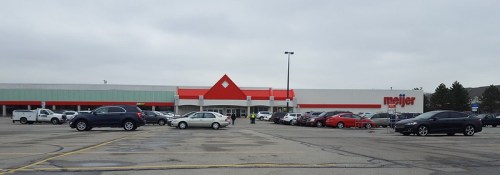 A Meijer store with a red roof, surrounded by a parking lot filled with various cars under a cloudy sky.