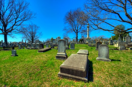 A peaceful cemetery with various gravestones and trees under a clear blue sky.