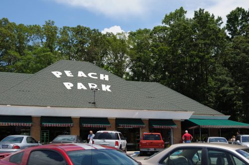A building with a sign reading "Peach Park," surrounded by trees and parked cars on a sunny day.