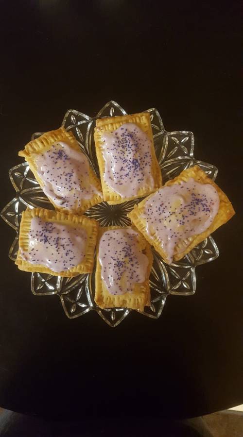 A glass plate holding five frosted pastries with purple icing and blue sprinkles, arranged neatly.