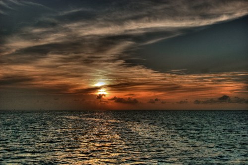 A serene sunset over the ocean, with vibrant orange and blue hues reflecting on the water and wispy clouds in the sky.