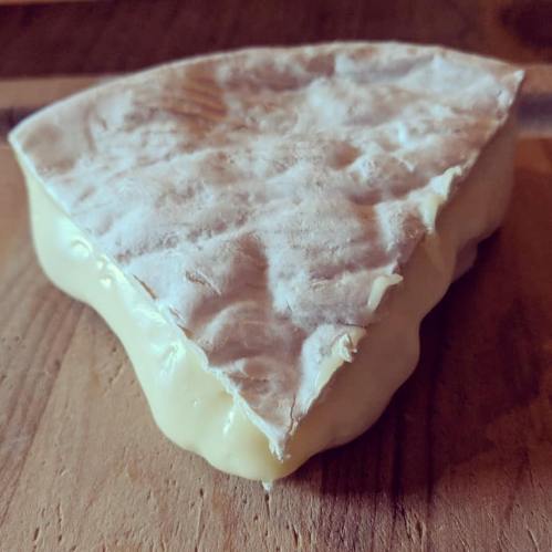 A wedge of soft cheese with a creamy texture, resting on a wooden surface.