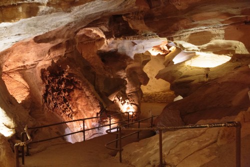 A dimly lit cave interior with rock formations and a winding path, illuminated by soft lights.