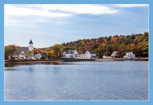 A serene waterfront scene featuring colorful autumn trees and charming houses along the shore.