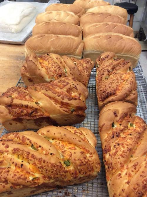 Freshly baked loaves of bread, including twisted cheese bread and classic white loaves, cooling on a wire rack.