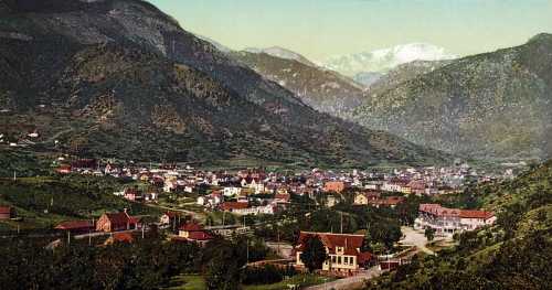 A scenic view of a valley town surrounded by mountains, featuring colorful buildings and lush greenery.