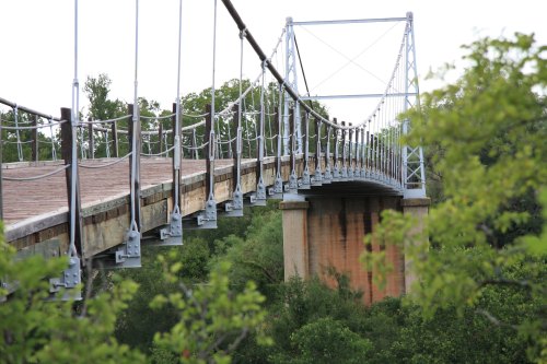 A suspension bridge spans over a river, surrounded by lush greenery and trees.