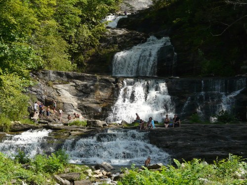 A scenic waterfall surrounded by lush greenery, with people enjoying the water and relaxing on the rocks.