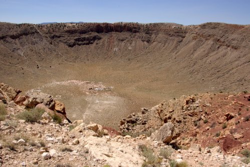 A vast, dry crater with rocky walls and a flat, barren floor under a clear blue sky.