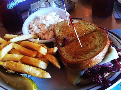 A plate featuring a sandwich with melted cheese, fries, coleslaw, and a pickle on the side.