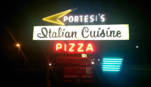 Neon sign for Portesi's Italian Cuisine featuring "Pizza" and "Air Conditioned" in bright colors at night.