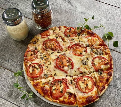 A freshly baked pizza topped with tomatoes, cheese, and herbs, served with grated cheese and red pepper flakes.