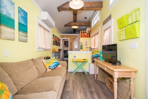 Cozy living area with a beige sofa, bright yellow walls, and beach-themed decor, featuring a TV and a small dining table.