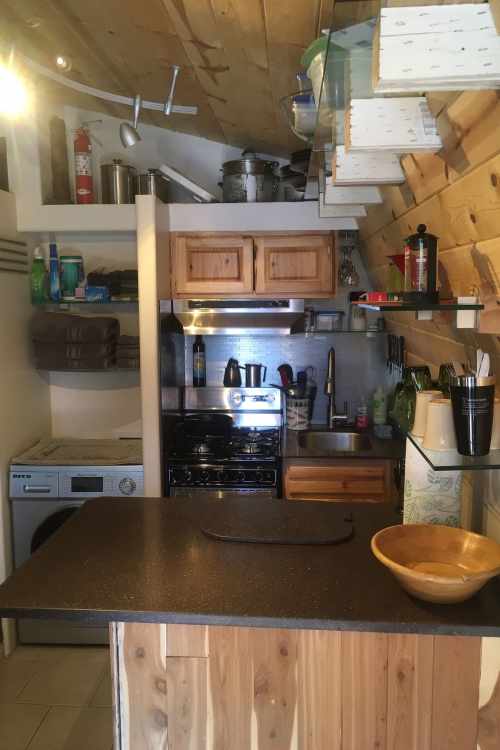 Cozy kitchen with wooden accents, featuring a stove, sink, and shelves filled with kitchenware and supplies.