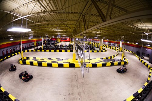 Aerial view of an indoor go-kart track with yellow and black barriers and karts racing around the circuit.