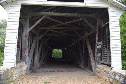 A view inside a weathered covered bridge with wooden beams and graffiti on the walls.