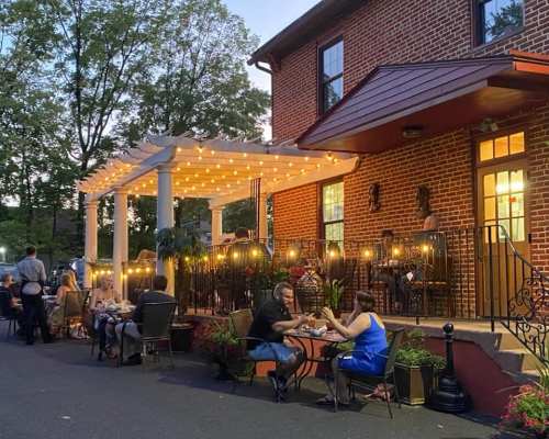 Outdoor dining scene at a cozy restaurant, with string lights and guests enjoying meals on a warm evening.