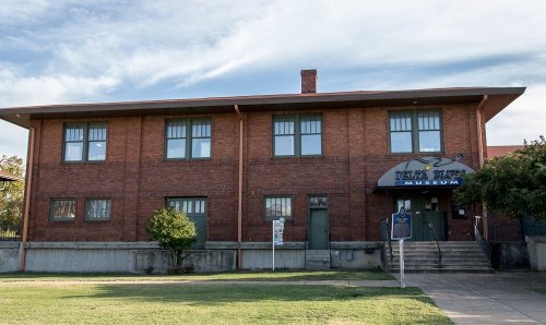 Exterior view of the Delta Blues Museum, a brick building with green windows and a sign, surrounded by grass.