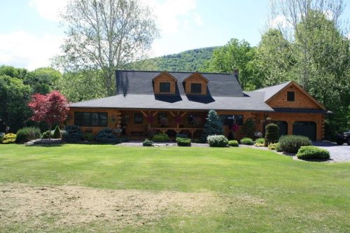 A large wooden house surrounded by lush greenery and colorful flowers on a sunny day.