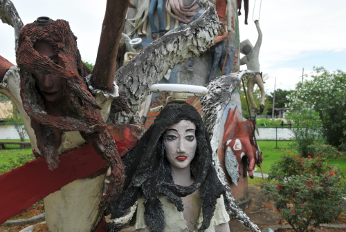 A surreal sculpture featuring a woman with dark hair, surrounded by abstract figures and vibrant colors in a garden setting.