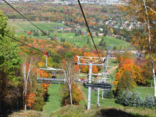 A scenic view from a ski lift, showcasing vibrant autumn foliage and a valley with a golf course below.