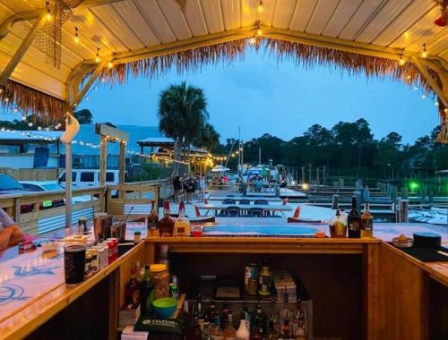 View from a bar with a thatched roof, overlooking a marina at dusk, with boats and palm trees in the background.