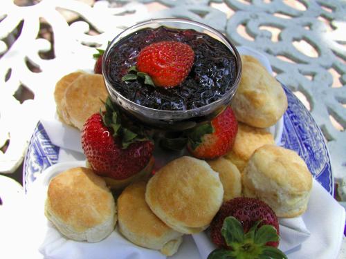 A plate of freshly baked biscuits surrounded by strawberries and a bowl of dark berry jam.