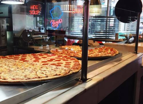 A display of large pizzas, one with pepperoni and the other with various toppings, in a restaurant setting.