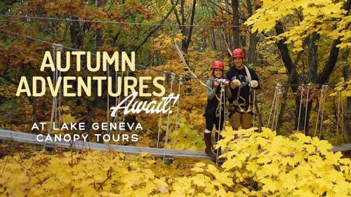 Two people in helmets stand on a zip line platform surrounded by vibrant autumn foliage at Lake Geneva Canopy Tours.