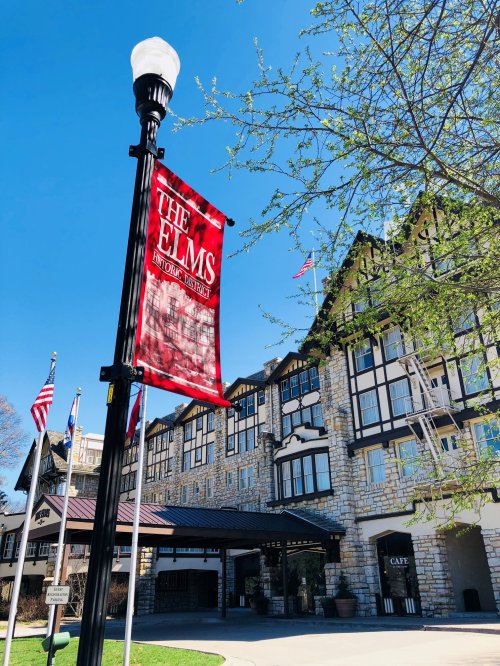 A historic building with a red banner reading "The Elms" and flags, set against a clear blue sky.