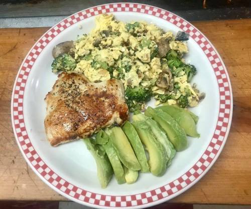 A plate with scrambled eggs mixed with vegetables, a grilled chicken breast, and sliced avocado.
