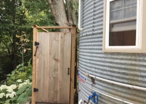 A wooden door next to a corrugated metal structure, surrounded by greenery and trees.