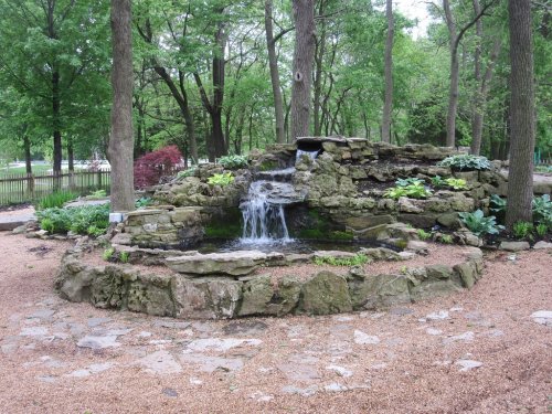 A serene stone waterfall surrounded by greenery and trees in a peaceful garden setting.