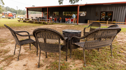 A circle of wicker chairs around a small table, with a building and picnic area in the background.