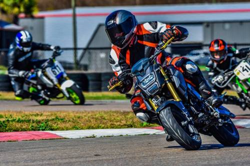 A motorcyclist leans into a turn on a racetrack, with other riders in the background. Brightly colored gear and bikes.