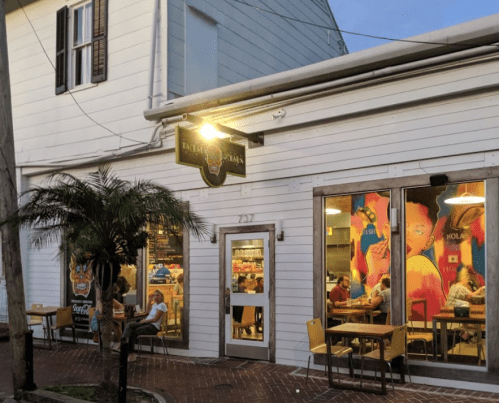 A cozy restaurant exterior with colorful murals, outdoor seating, and patrons dining inside.