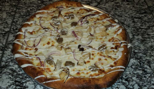 A large pizza topped with chicken, red onions, and drizzled with white sauce on a golden crust.